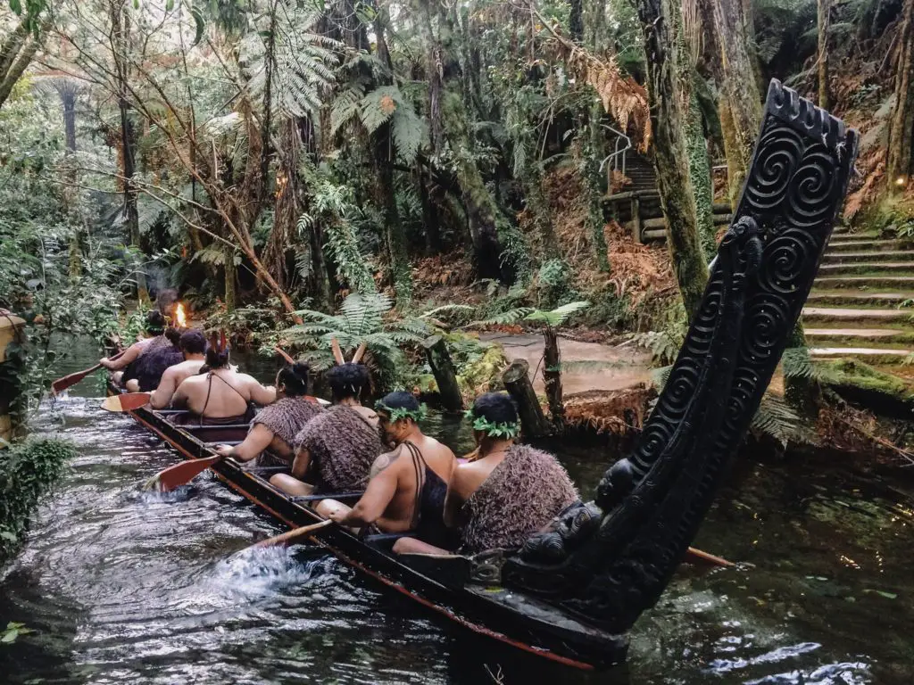Warriors in traditional dress paddle an ancient canoe
